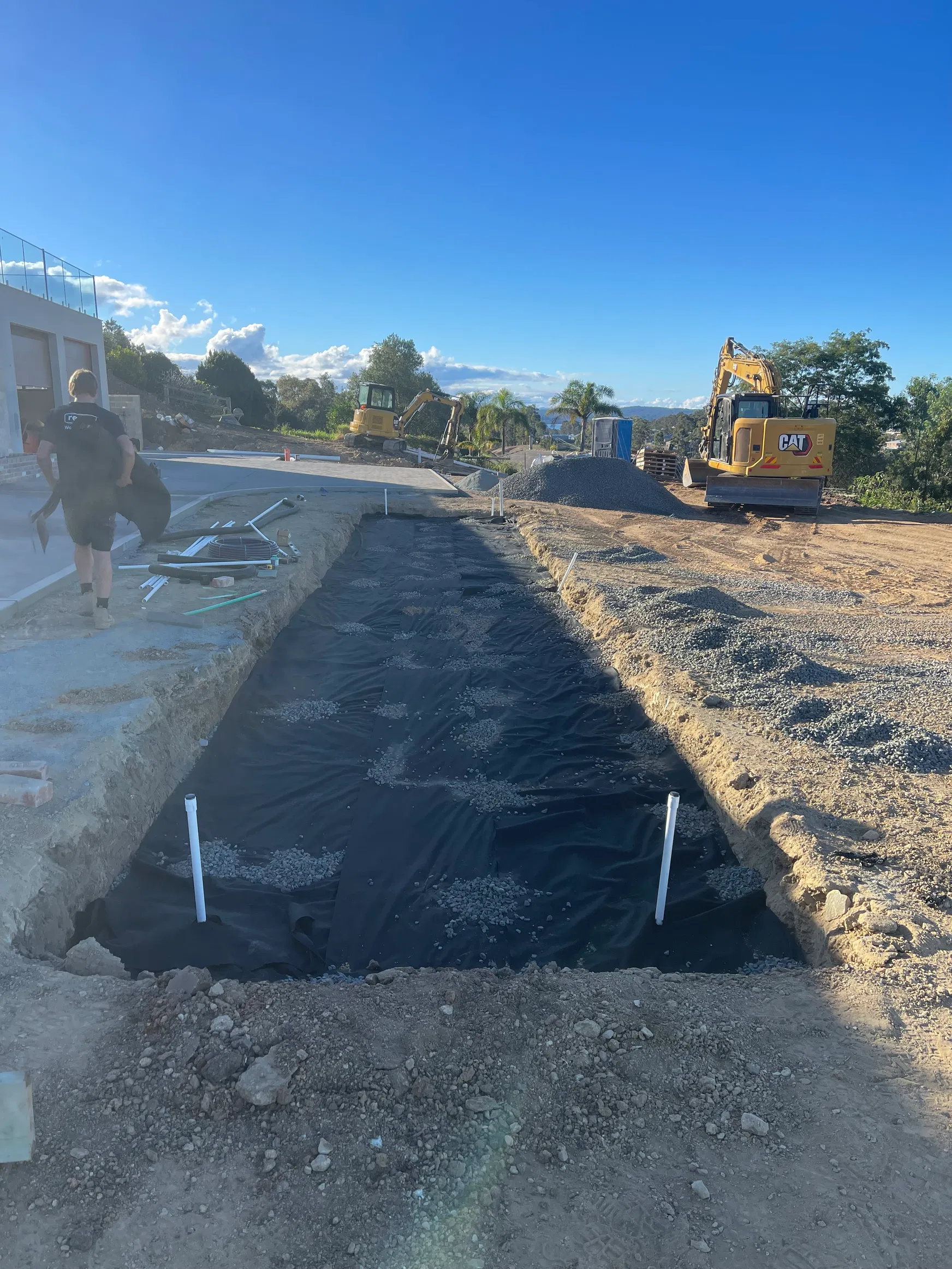 Fabric-lined trench with PVC risers and excavators on residential site