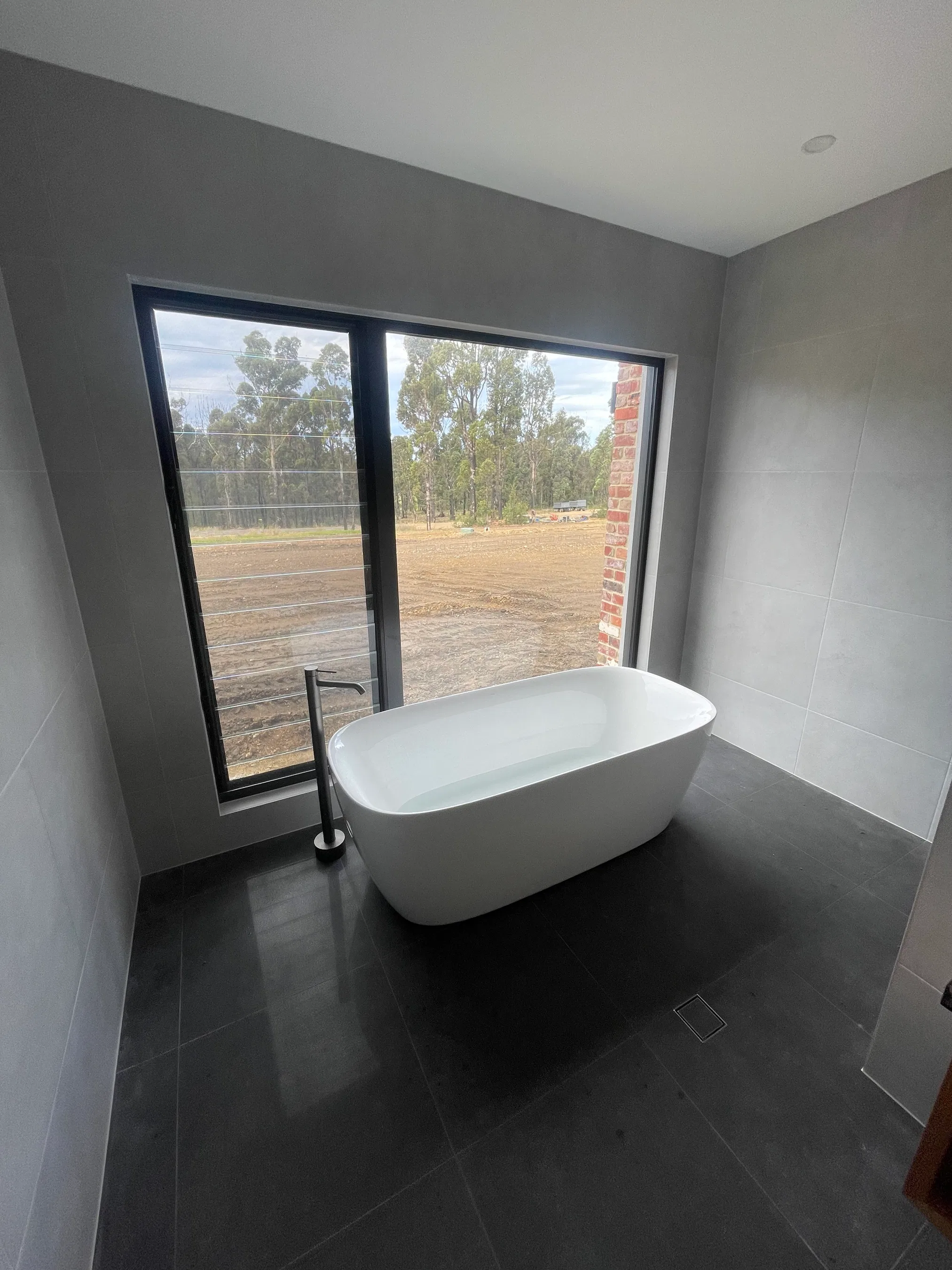 White freestanding bathtub on dark grey tiles with floor-mounted mixer