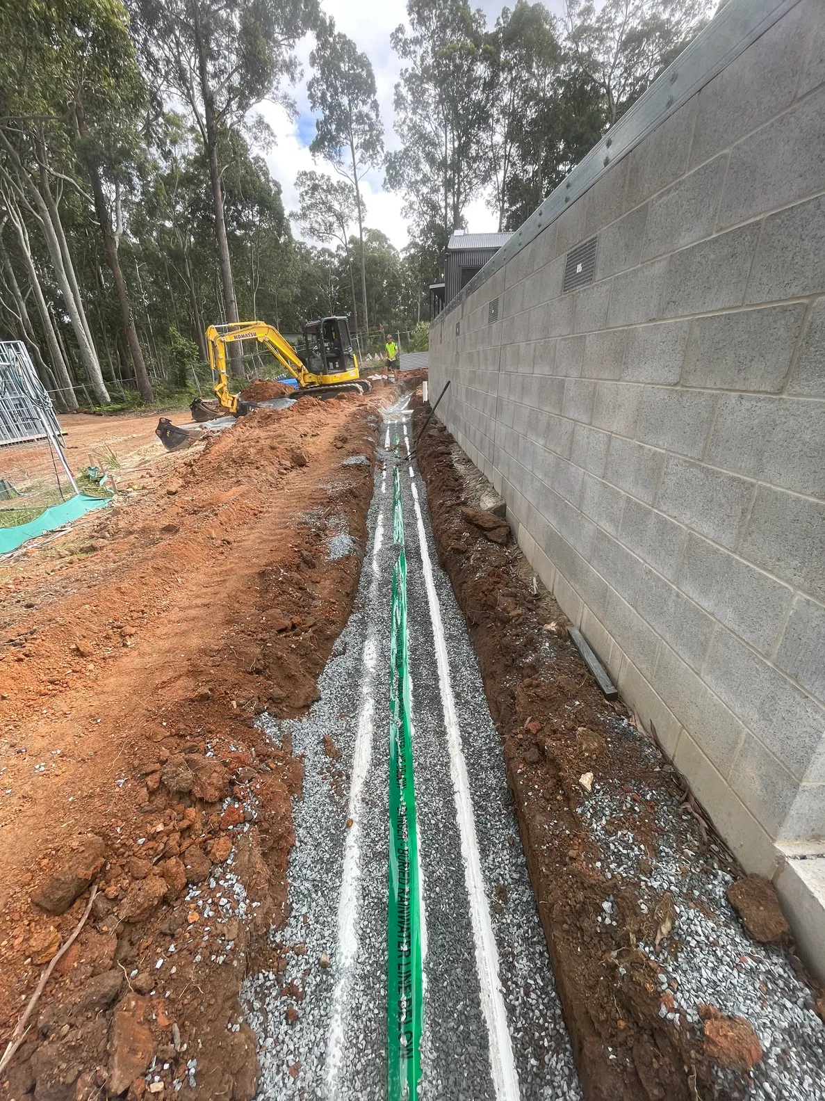 Stormwater and utility pipes laid in trench beside new masonry wall with excavator on site