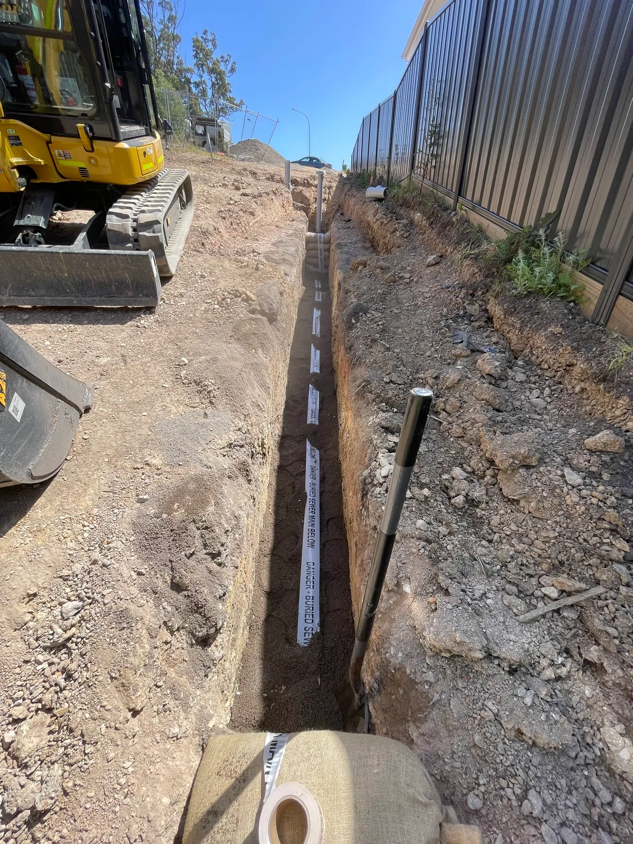 Sewer main trench excavation with buried sewer warning tape on residential site